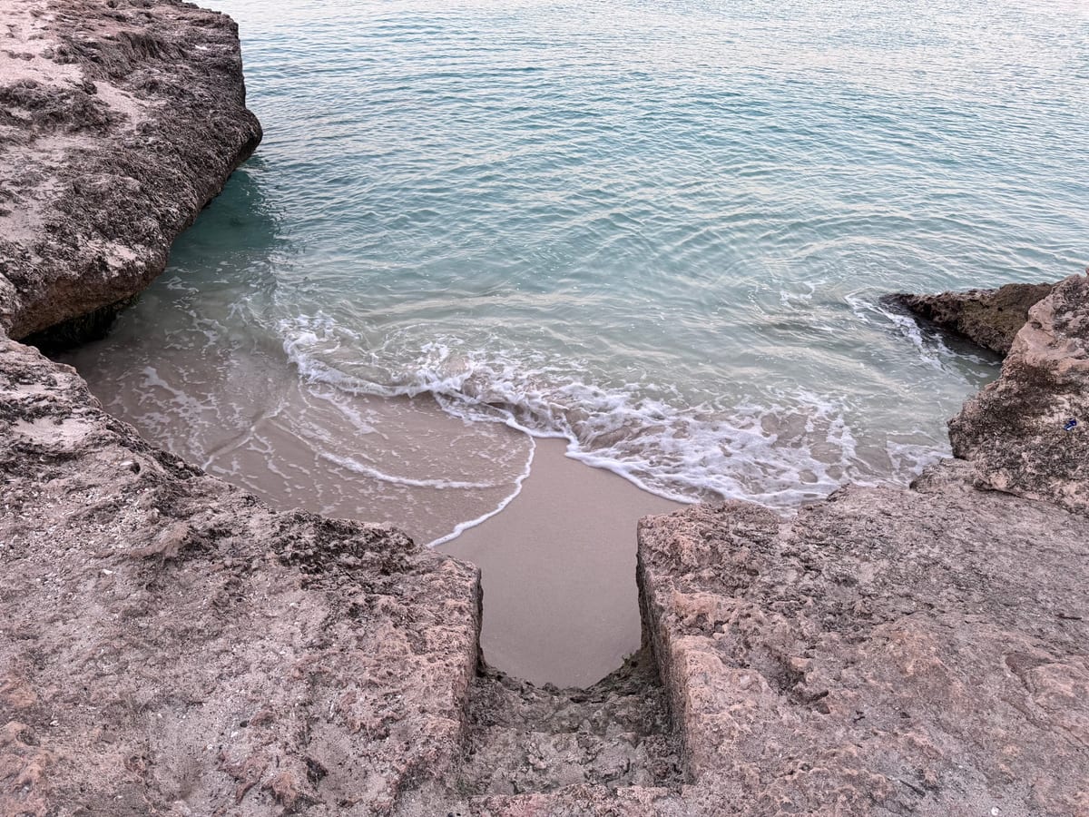 Original ground-level close photograph of the narrow sandy Tres Trapi water entry between rocks
